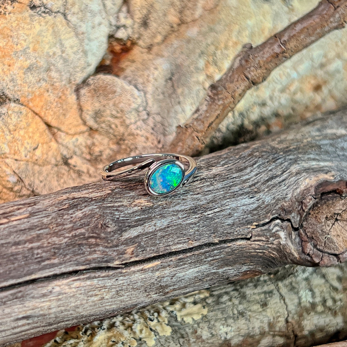 Slanted oval opal doublet ring in silver on driftwood against Australian sandstone