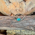 Slanted oval opal doublet ring in silver photographed in profile on driftwood, showing the setting