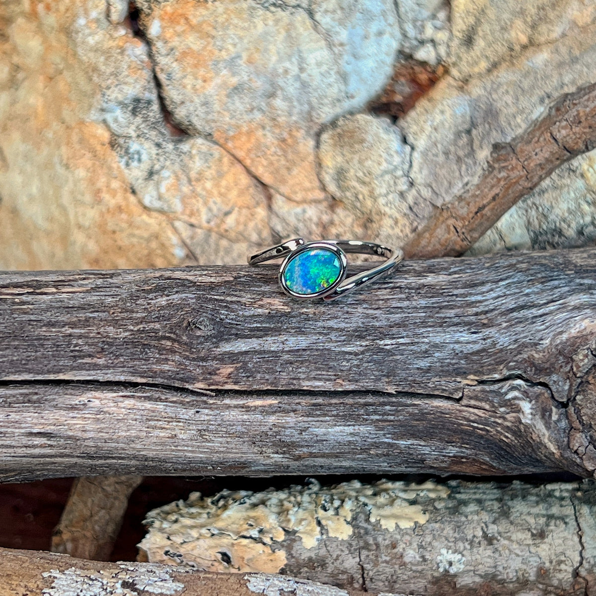 Slanted oval opal doublet ring in silver on driftwood, the oval opal doublet catching the light