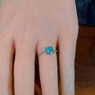 Slanted oval opal doublet ring in silver worn on the hand, viewed across the fingers