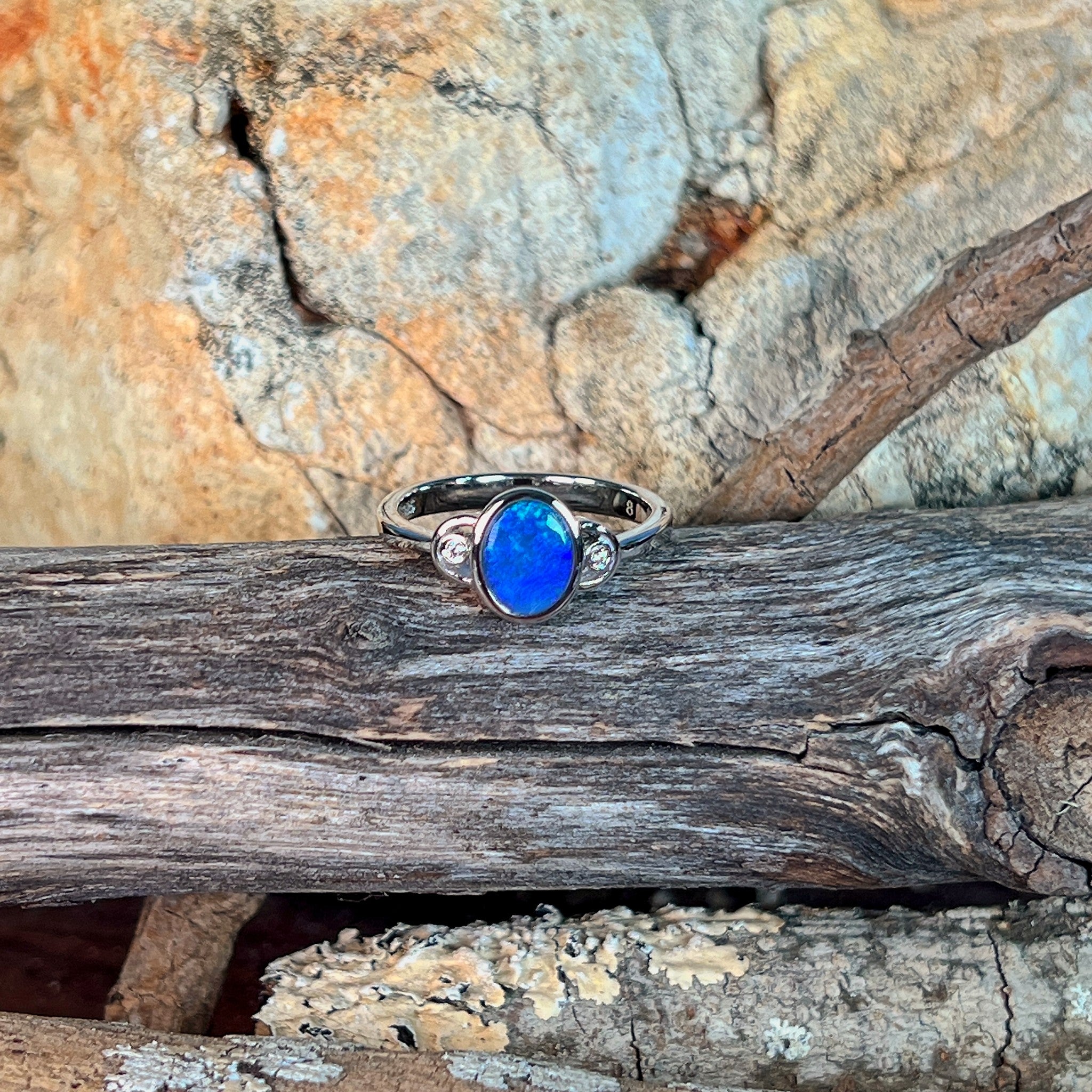 Blue opal doublet ring in silver on driftwood, the oval opal doublet catching the light