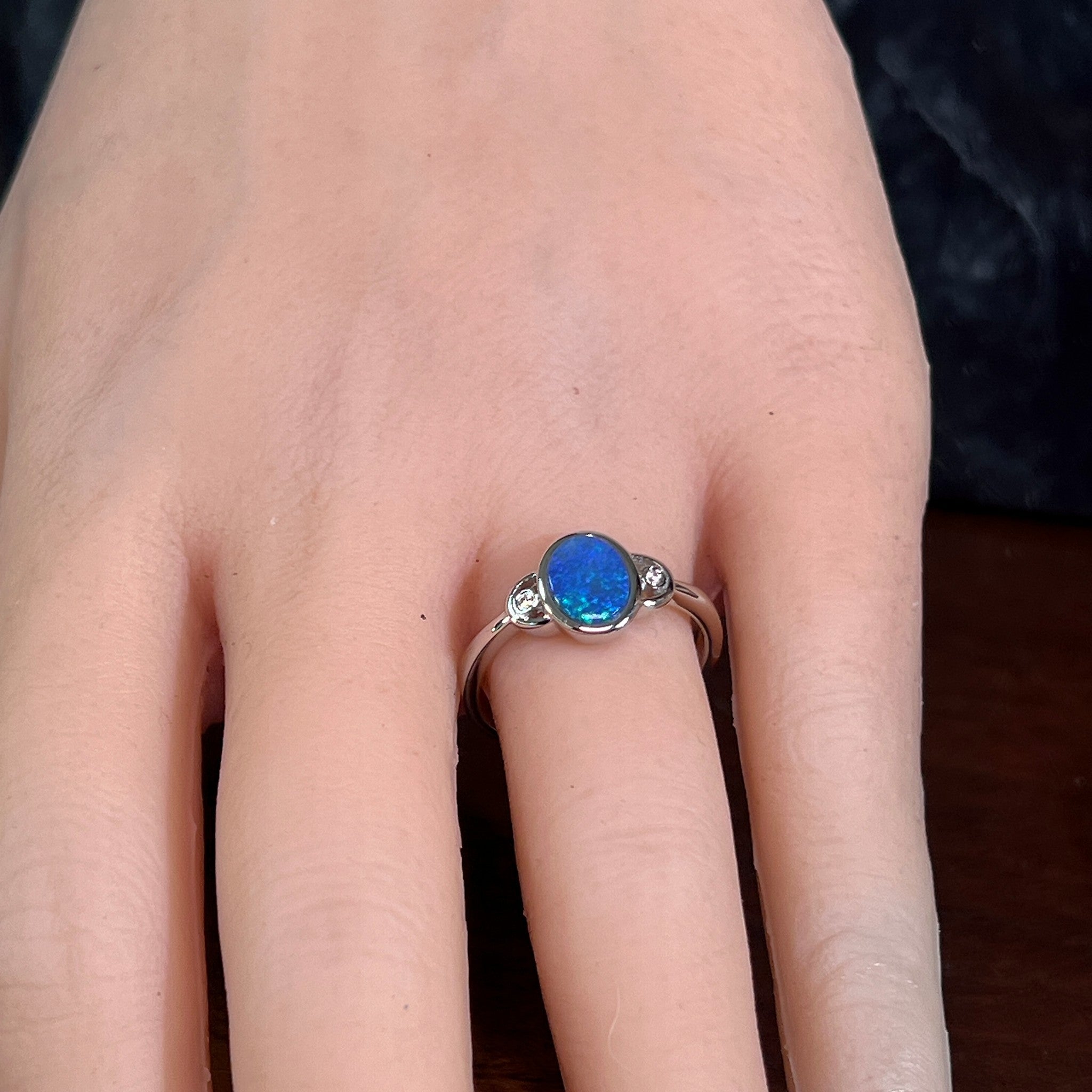 Blue opal doublet ring in silver worn on the hand, viewed across the fingers