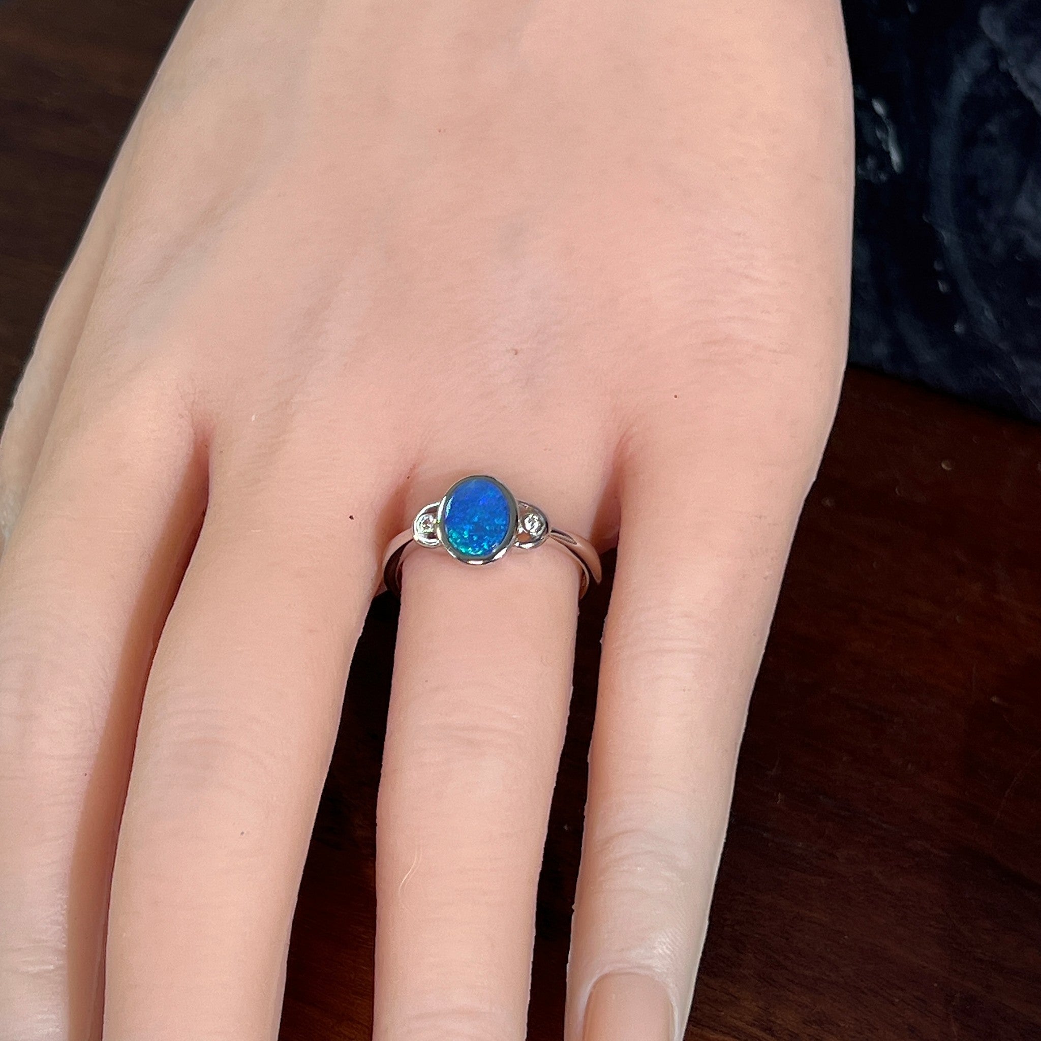 Blue opal doublet ring in silver on the hand, angled to catch the blue and green play of colour