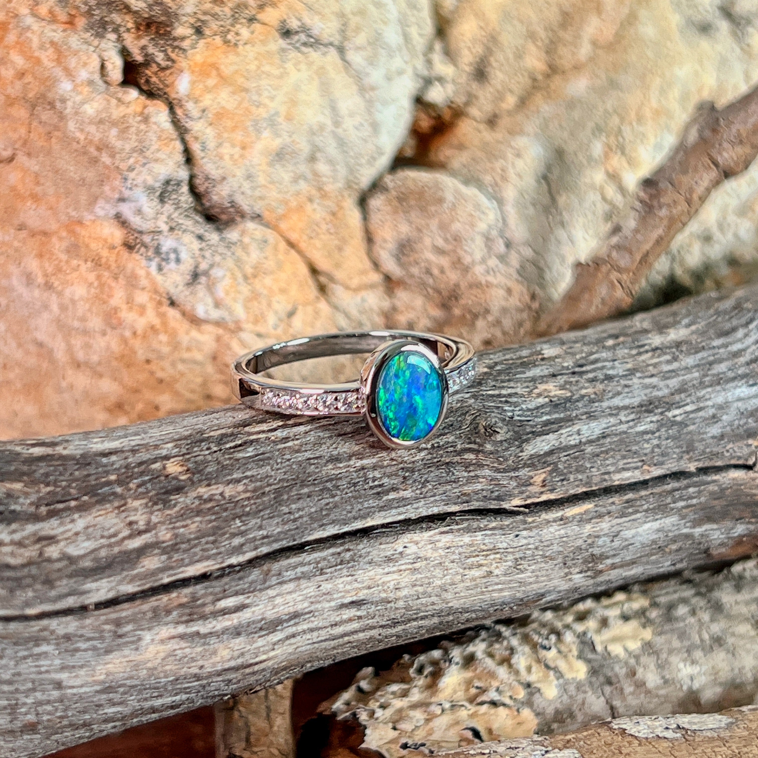Oval opal doublet ring with zirconia shoulders on driftwood against Australian sandstone