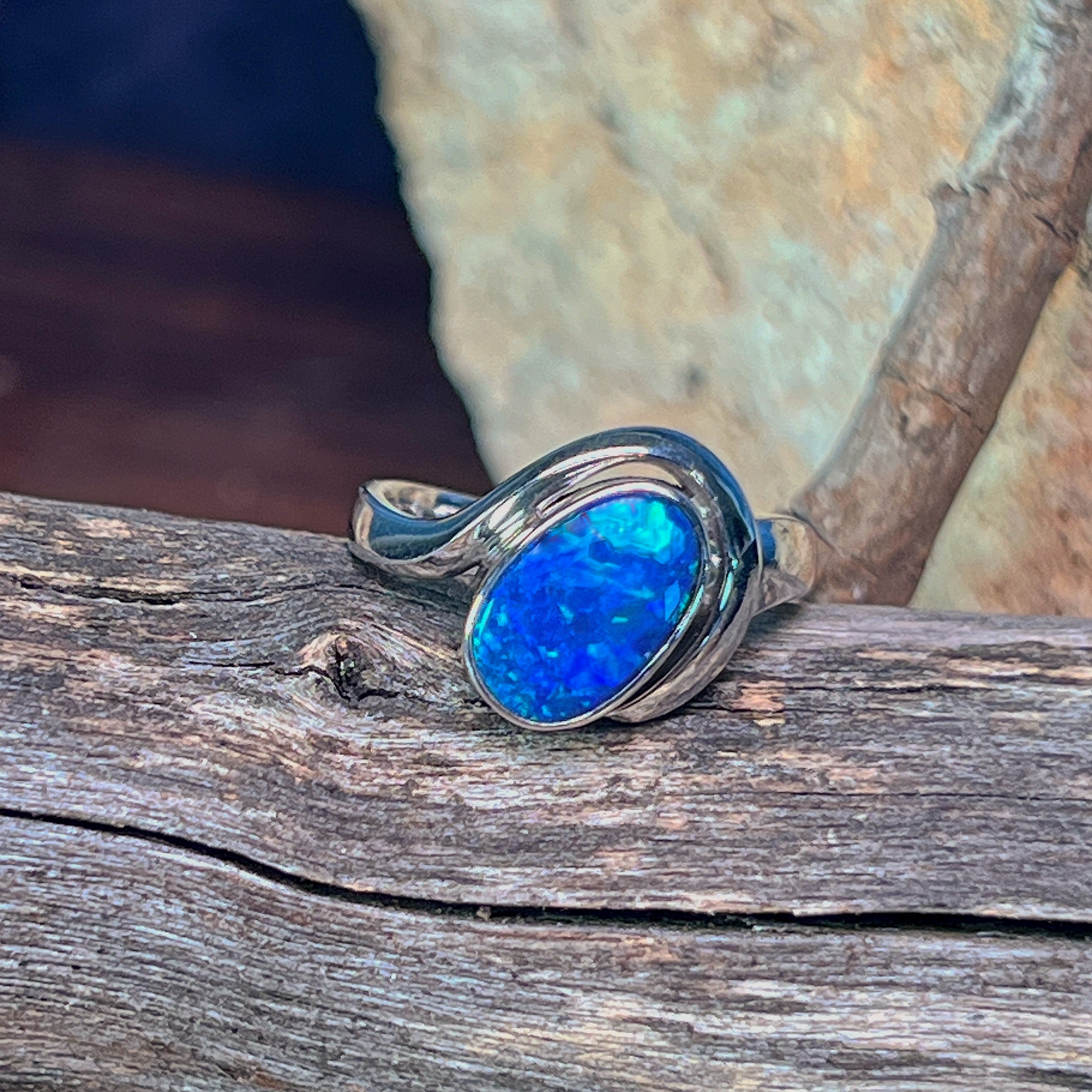Sterling silver oval opal doublet solitaire ring resting on weathered driftwood