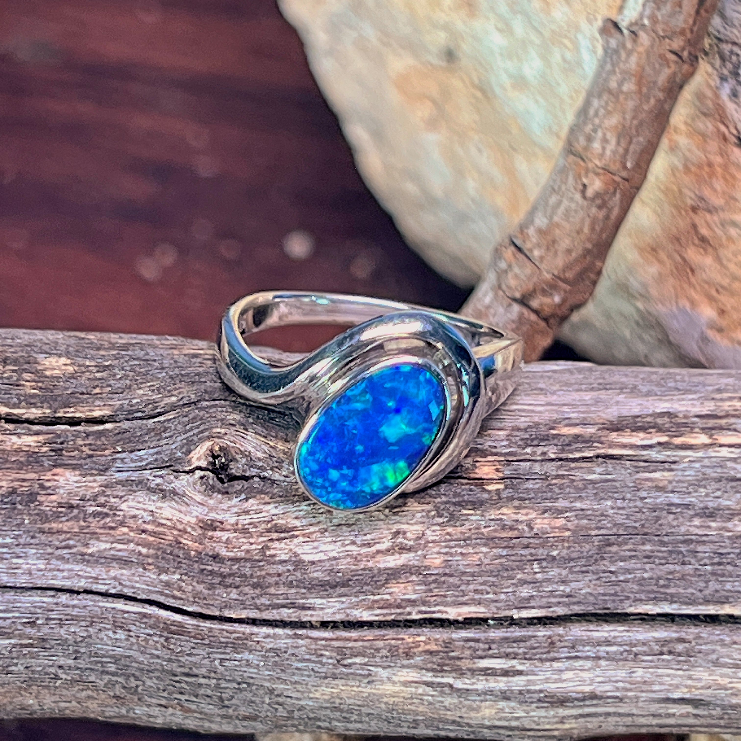 Modern silver opal doublet solitaire ring angled against driftwood and stone