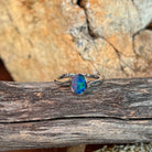 Oval opal doublet solitaire ring in silver resting on weathered driftwood
