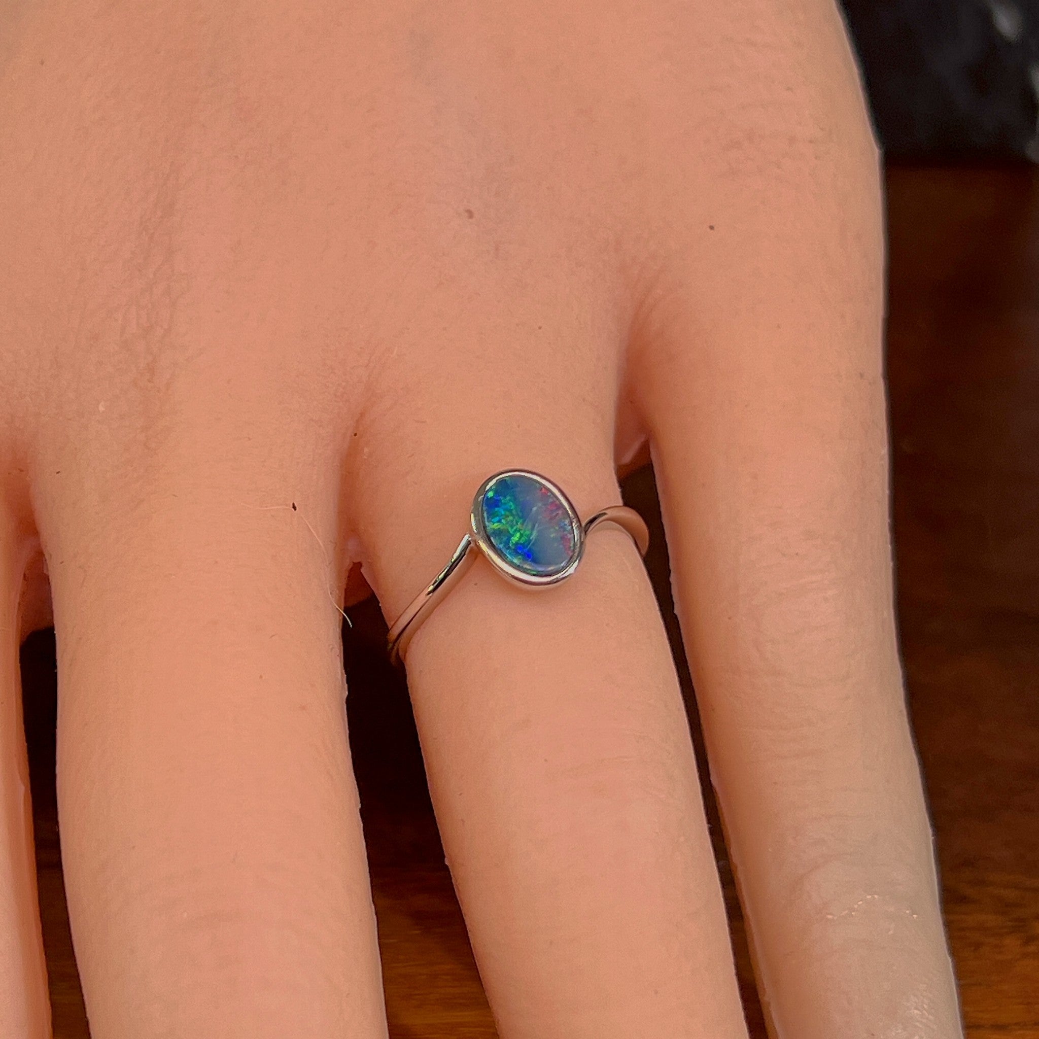Oval opal doublet solitaire ring in silver worn on the hand, full view across the fingers