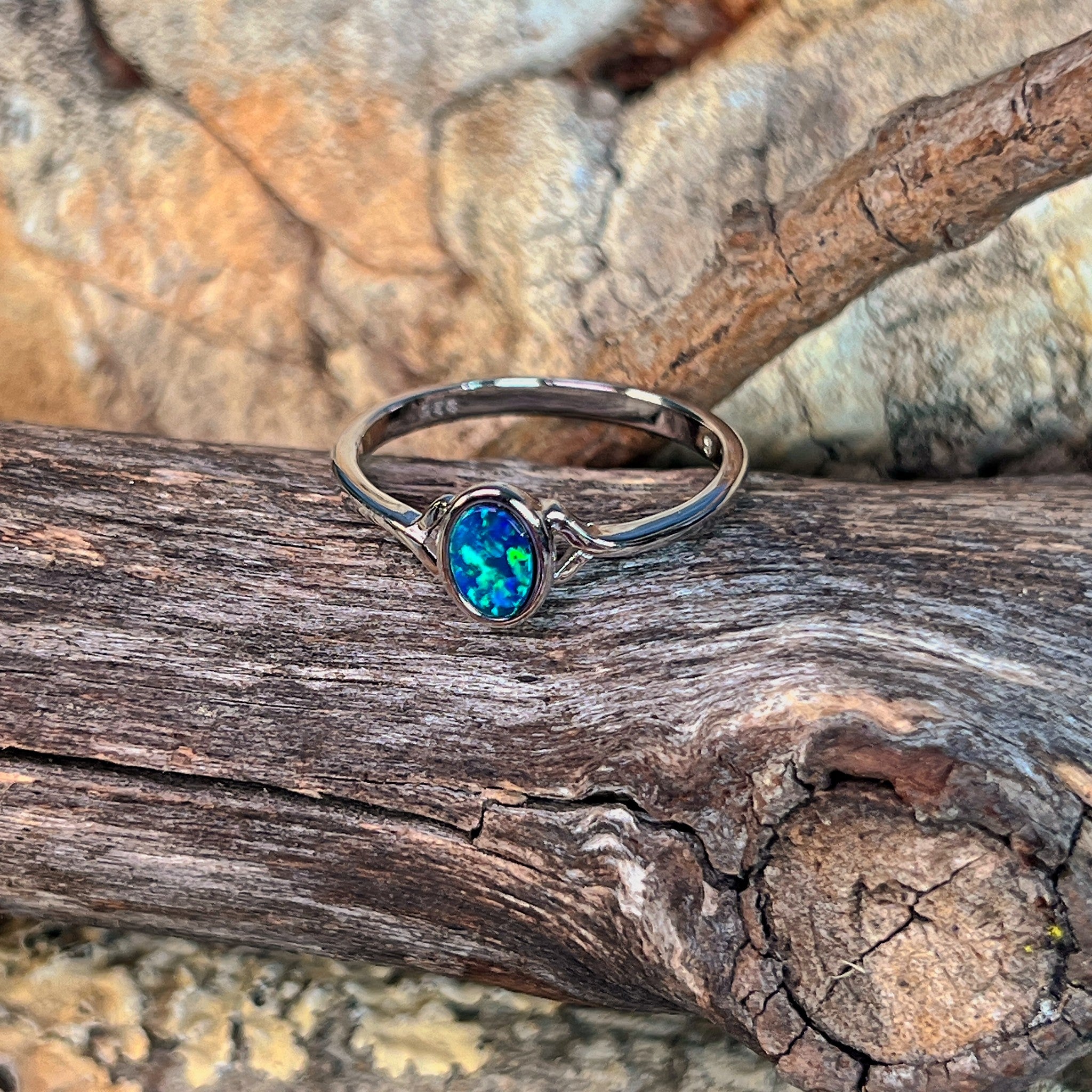 Deep green opal doublet ring in silver photographed in profile on driftwood, showing the setting