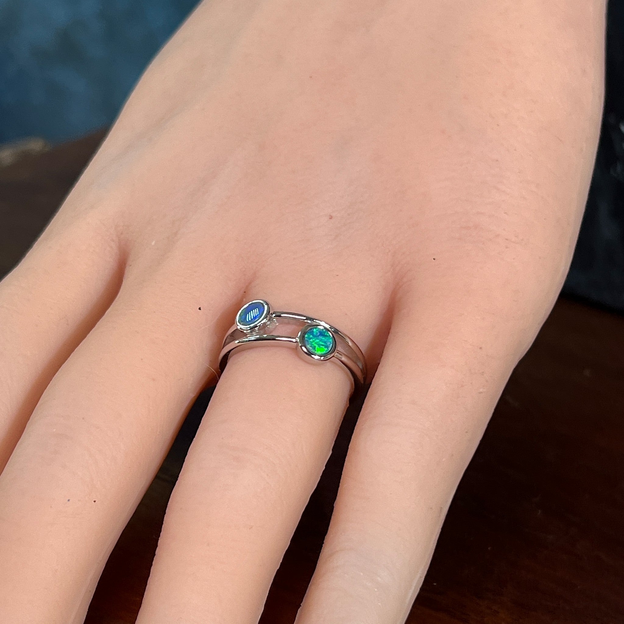 Silver ring with two round opal doublets on the hand, angled to catch the blue and green play of colour