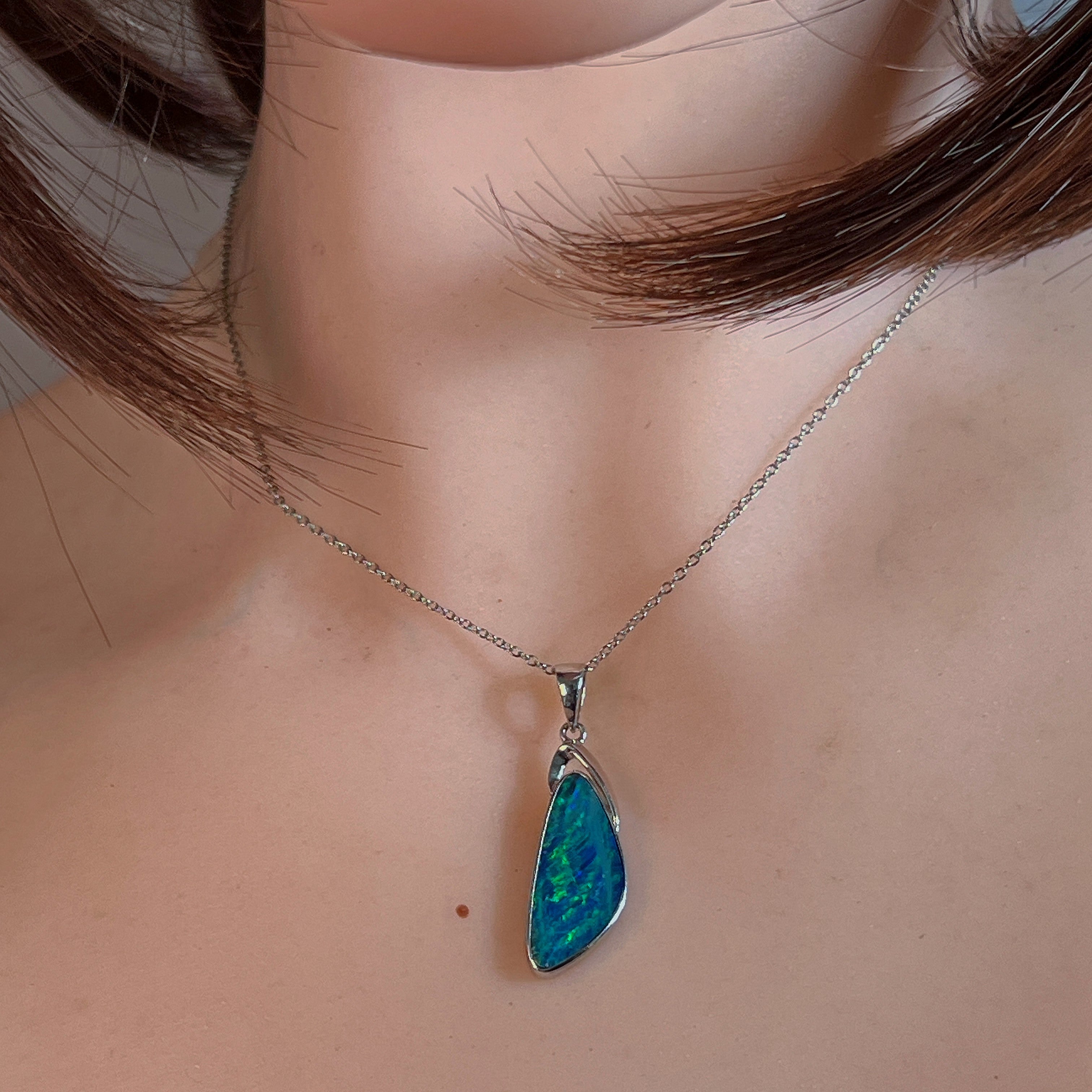 Triangular opal doublet pendant worn at the neck, showing its scale on the collarbone