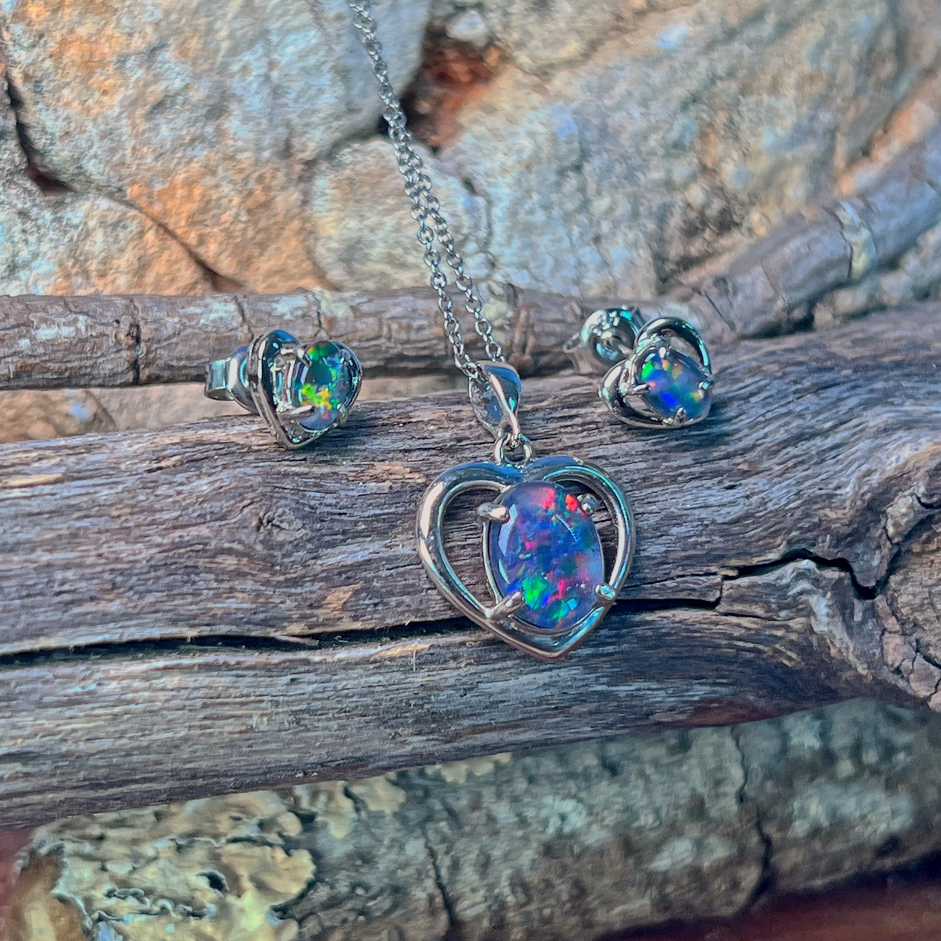 Opal triplet heart pendant and earrings in silver against driftwood and stone