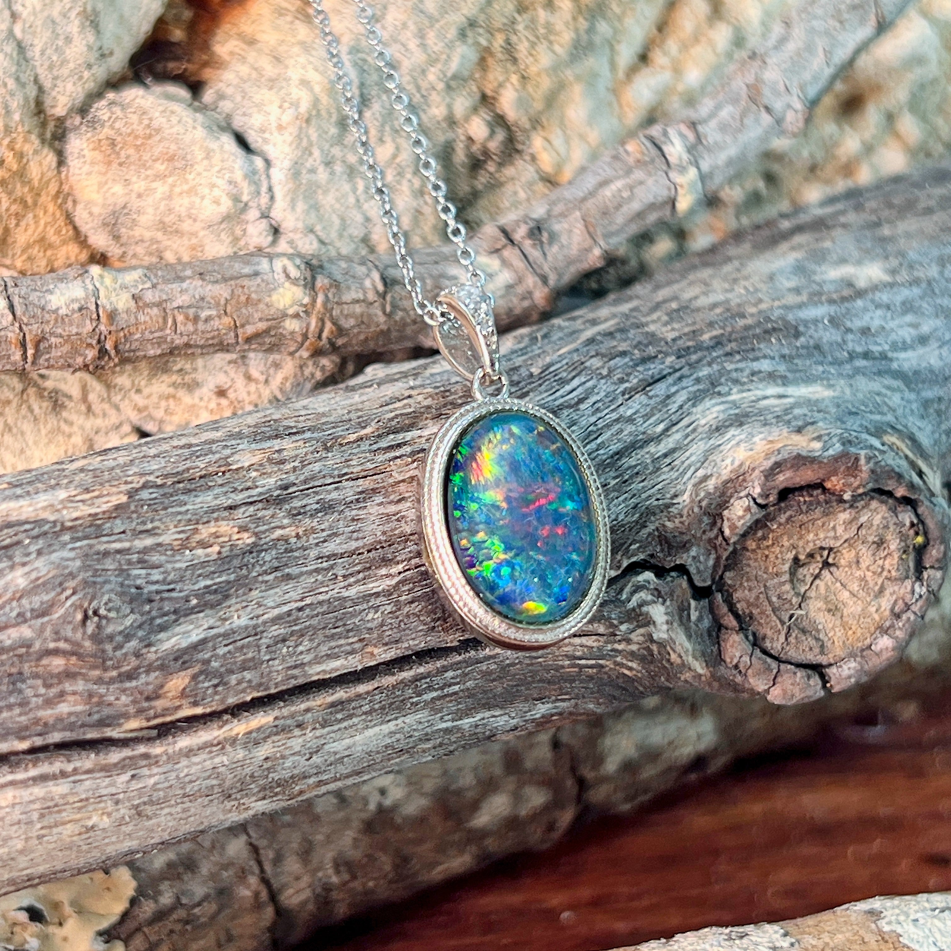 Oval opal triplet necklace with milgrain bezel detail, close view against driftwood