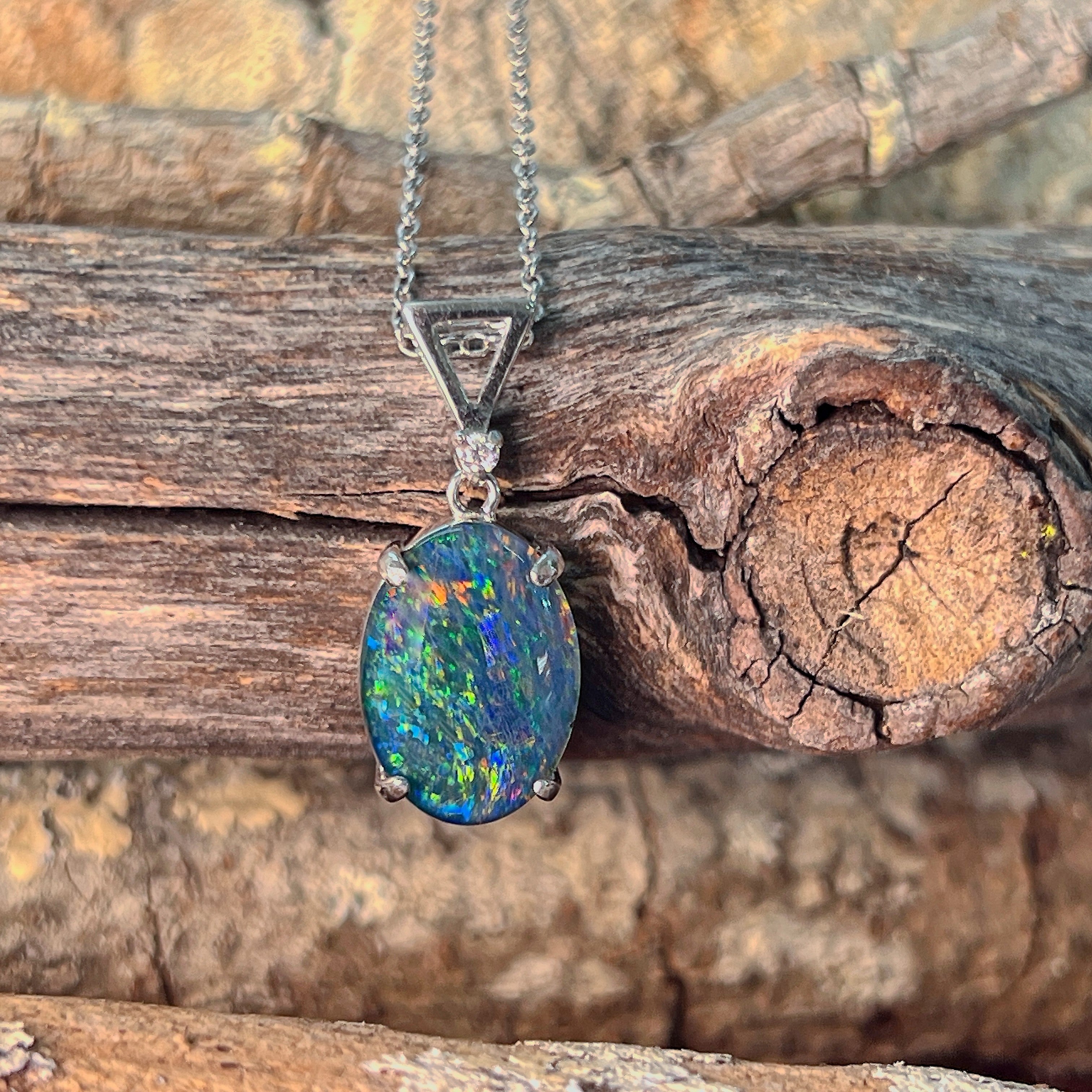 Sterling silver claw-set opal triplet pendant hanging against weathered driftwood