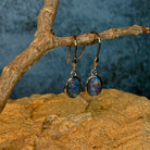 Angled view of sterling silver dangling earrings with 8x6mm oval opal triplets on a driftwood branch