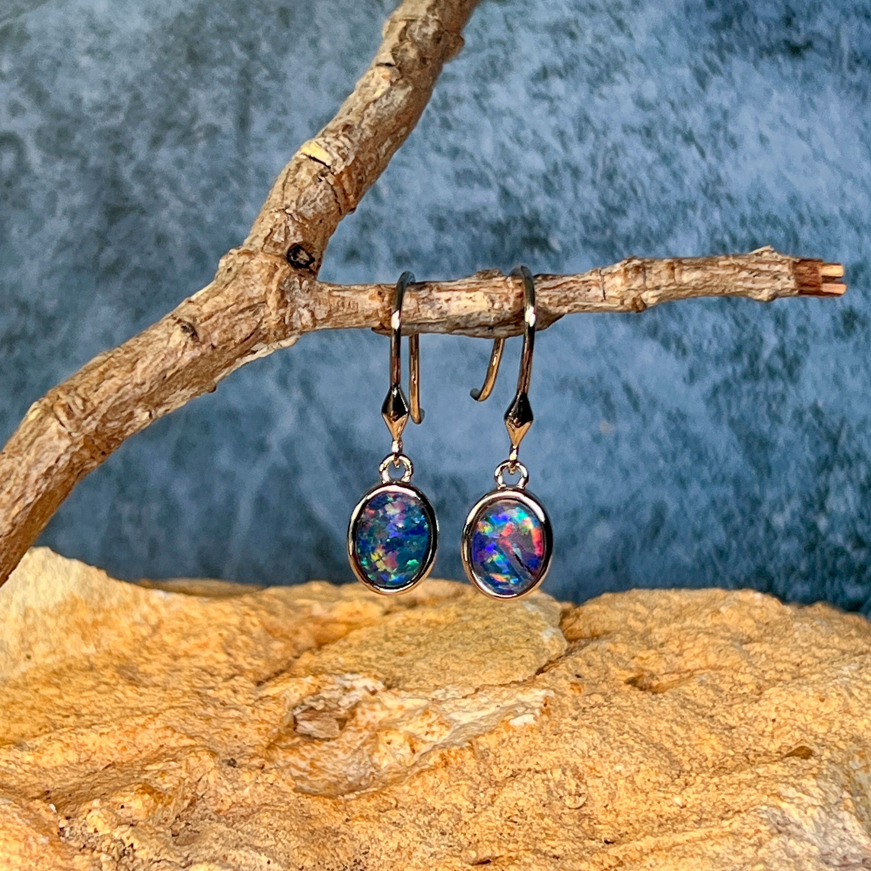 Sterling silver opal triplet dangling earrings side by side on driftwood, showing play-of-colour