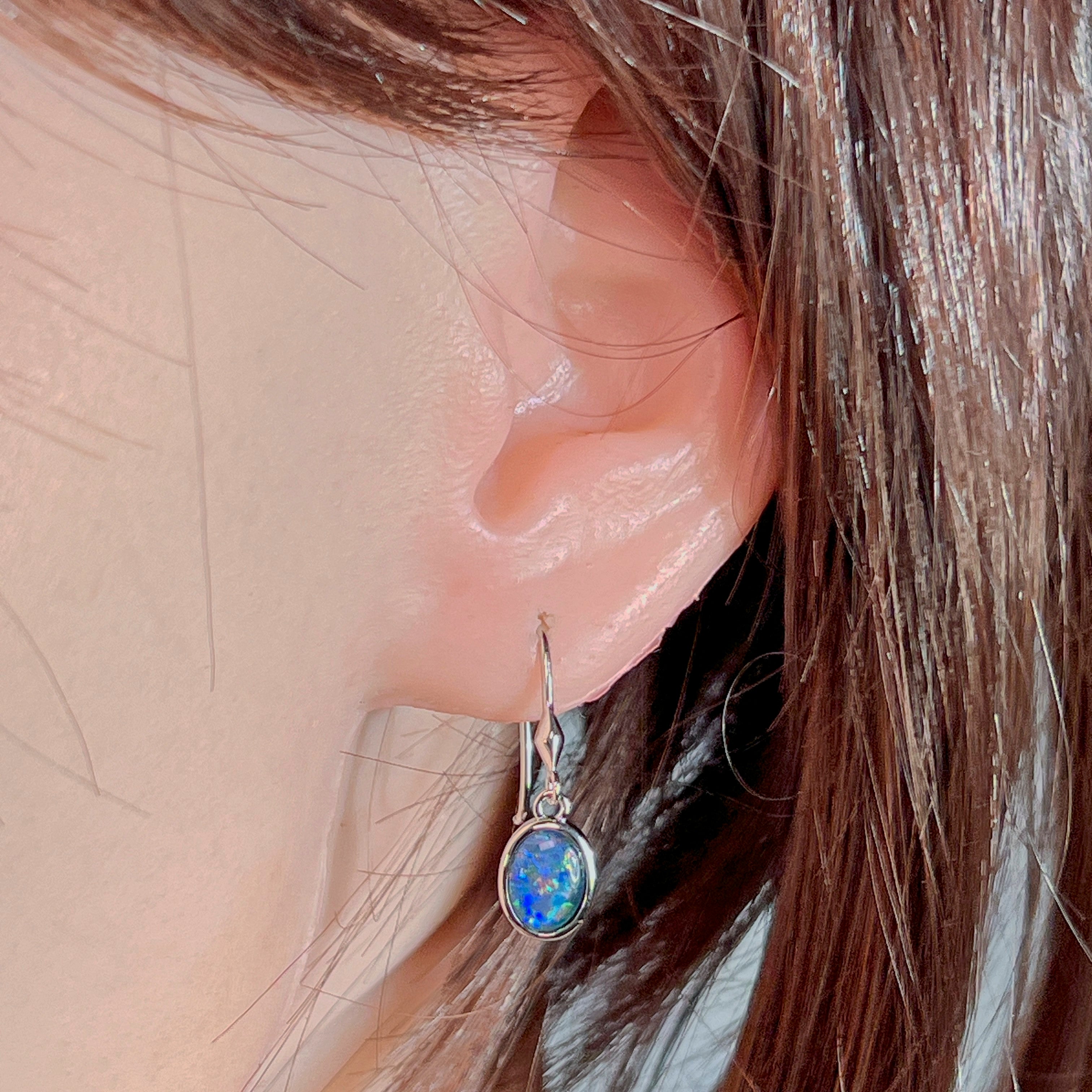 Ear close-up of the sterling silver dangling earring with oval Australian opal triplet