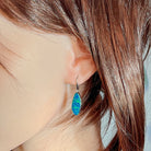 Green-blue opal doublet drop earring worn on the ear beneath loose hair
