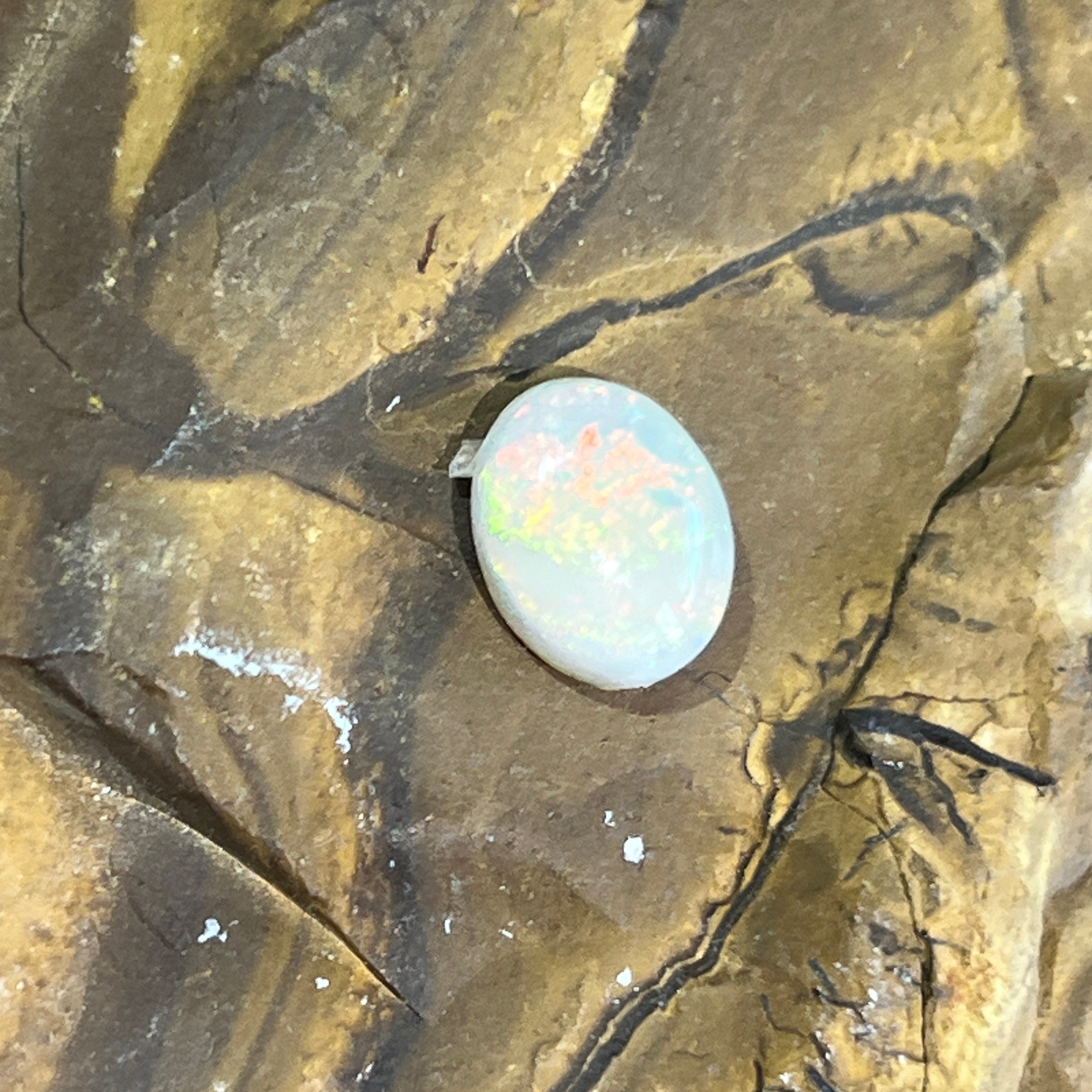 Australian white opal, 1.1ct oval cabochon, face up on ironstone in natural light