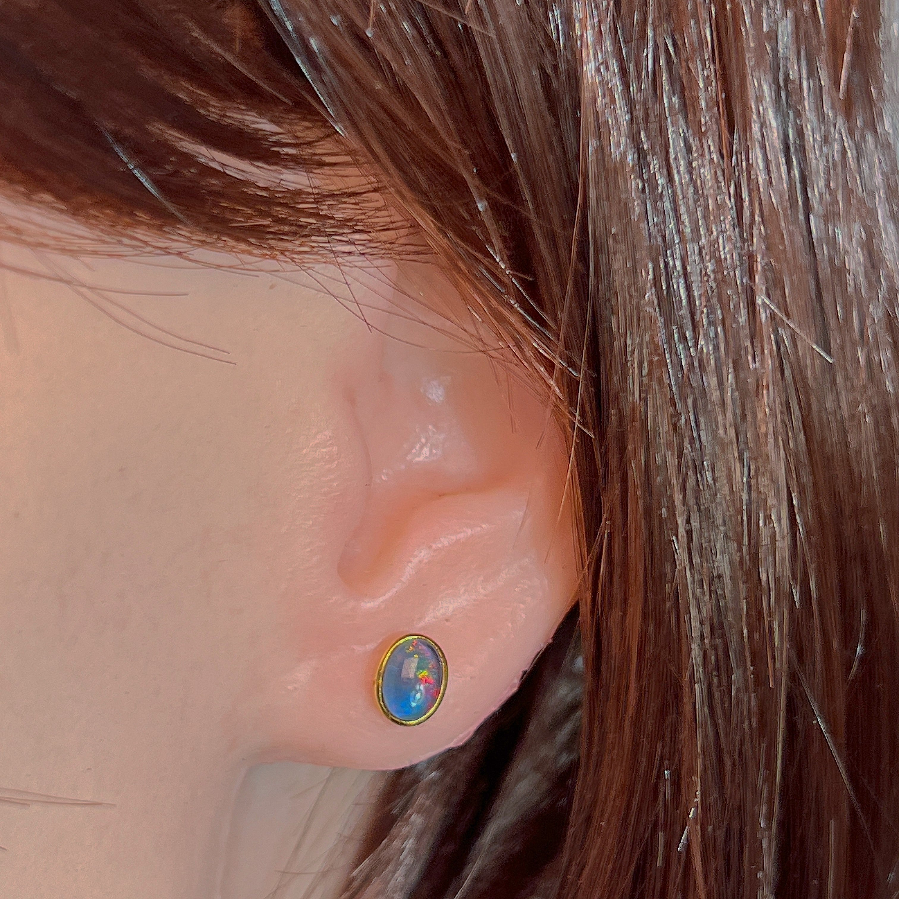 Bezel-set opal triplet stud earring worn on the ear, showing its scale on the earlobe