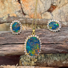 Gold-plated silver opal triplet halo pendant and earrings arranged on weathered driftwood