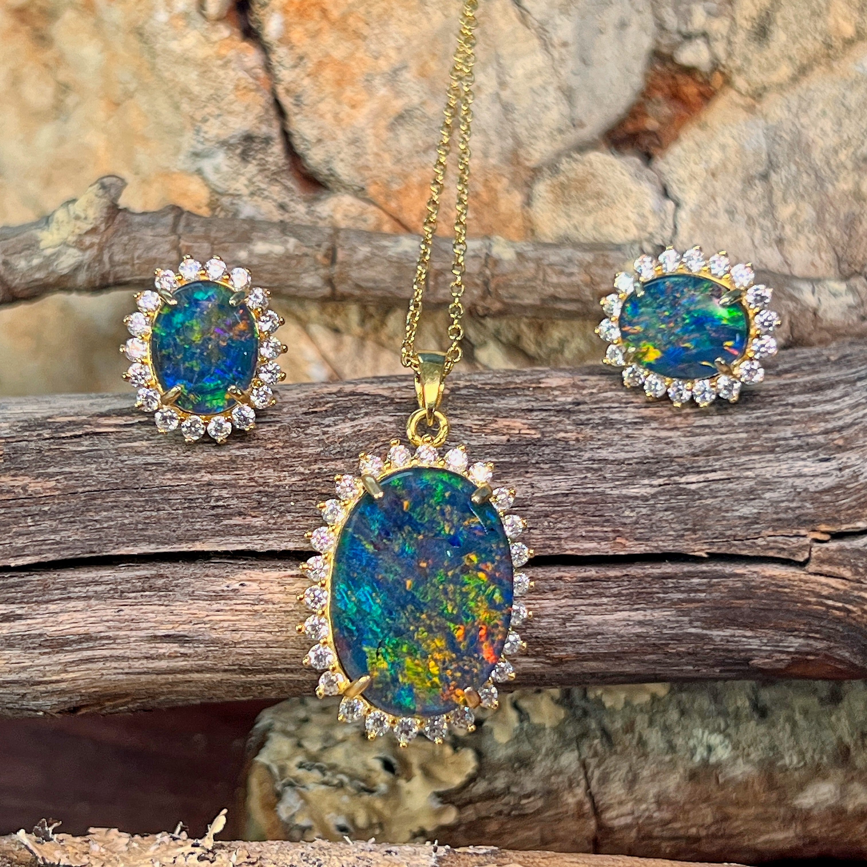 Gold-plated silver opal triplet halo pendant and earrings arranged on weathered driftwood