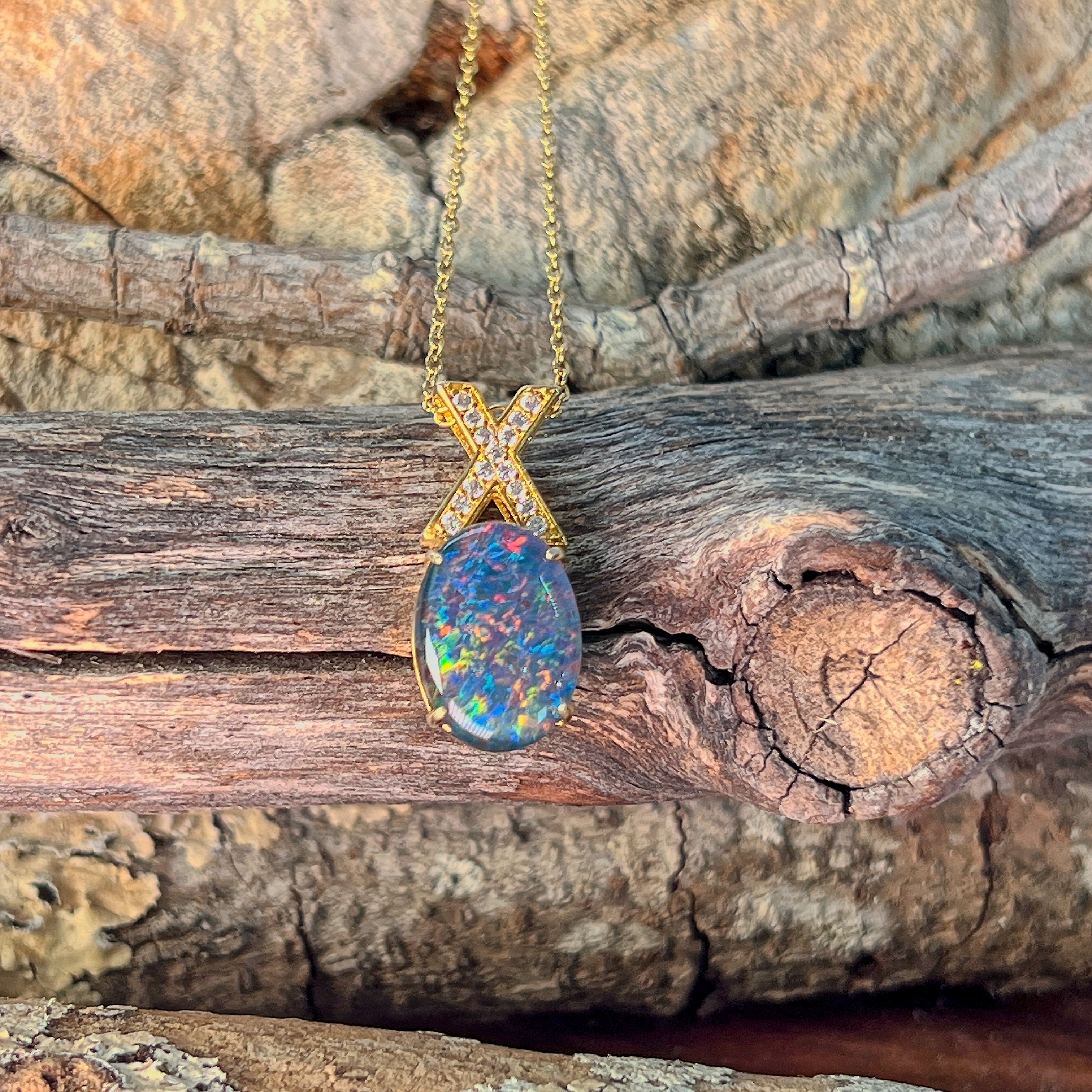 Oval opal triplet necklace in gold-plated silver angled against driftwood and sandstone