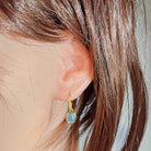 Ear close-up of the yellow gold plated dangling earring with oval Australian opal triplet