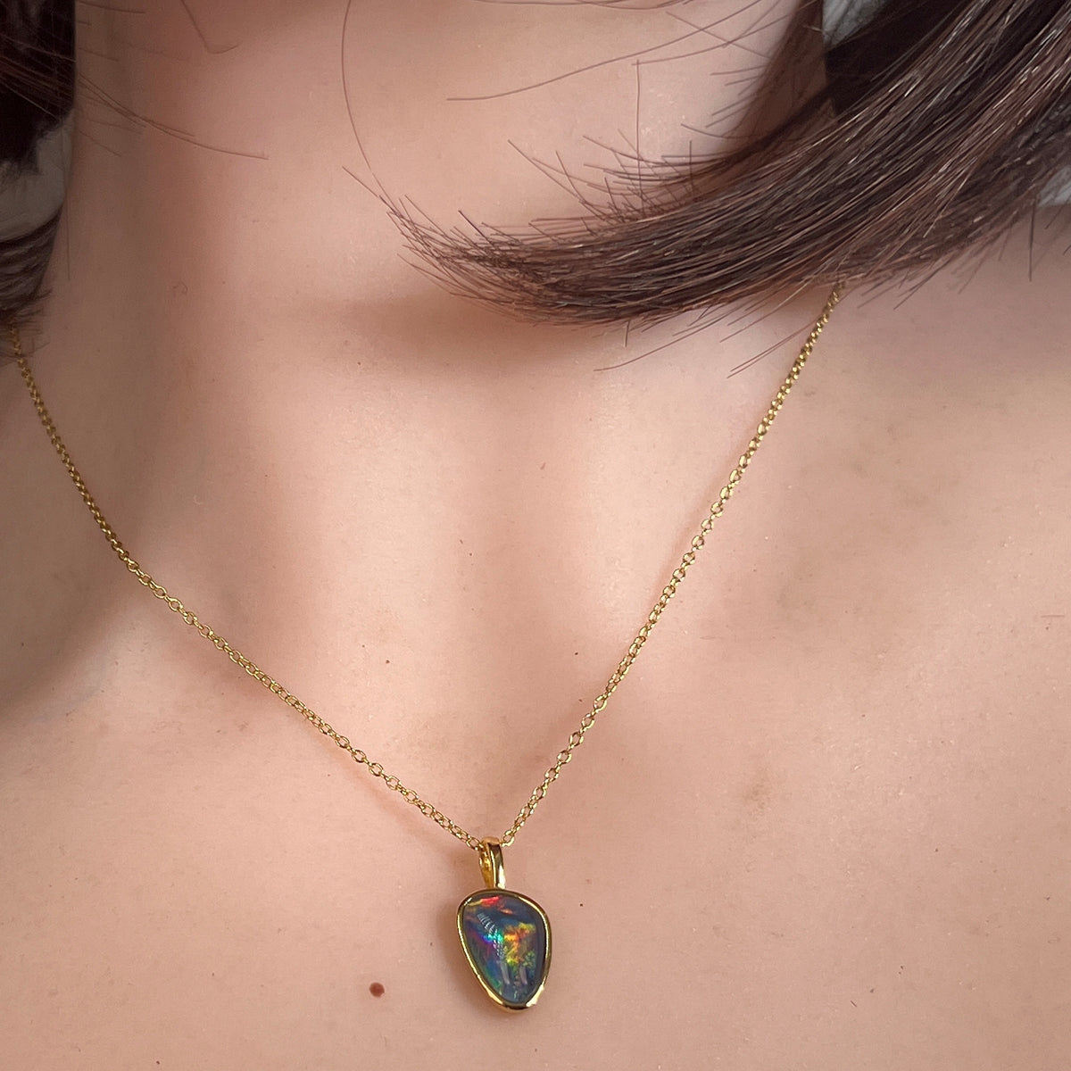 freeform Australian opal triplet pendant worn, yellow gold-plated silver, blue, red and green