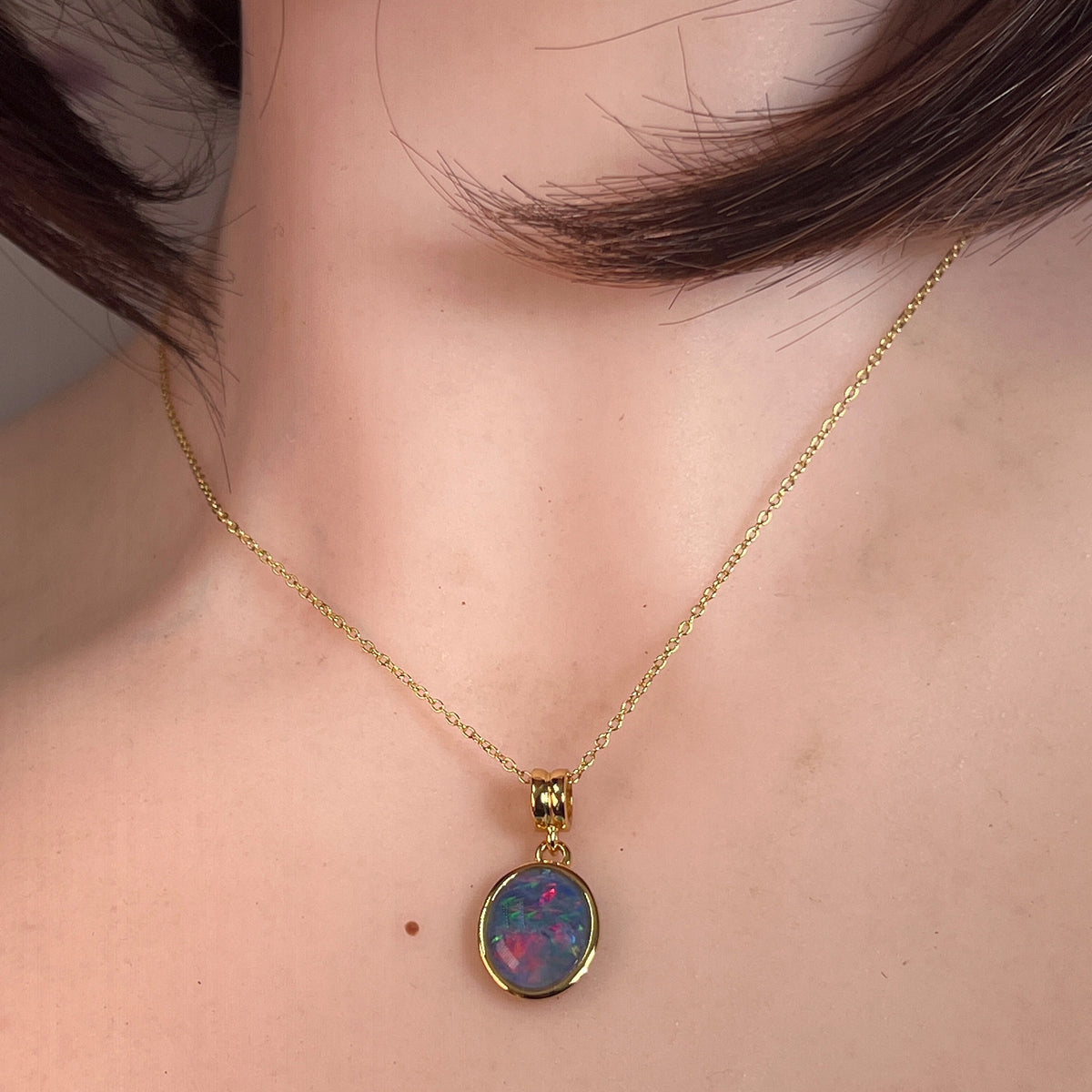 14 x 10mm oval Australian opal triplet pendant worn at the neck, yellow gold-plated silver